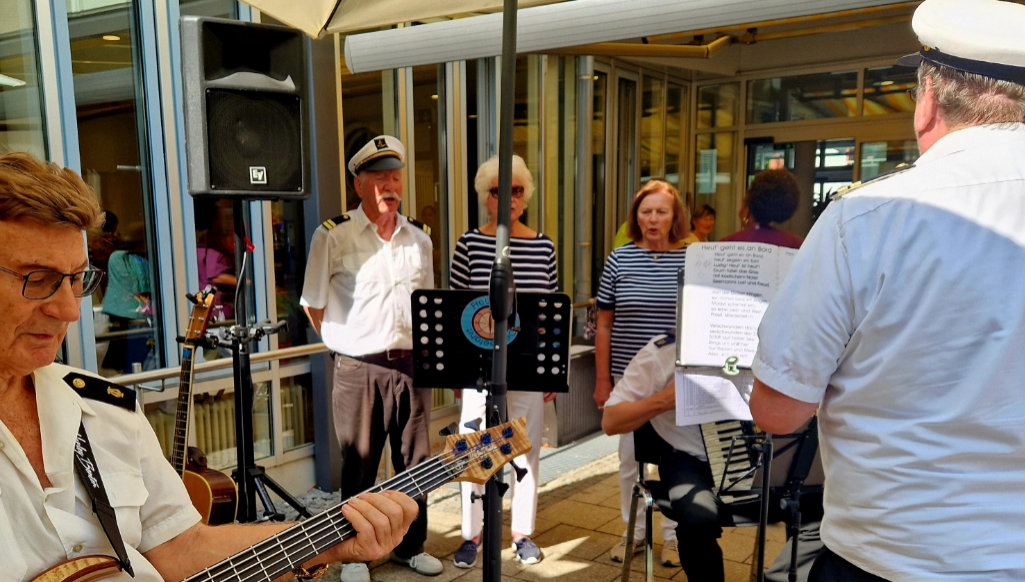 Menschen stehen im Halbkreis Singen und eine Band spielt Musik