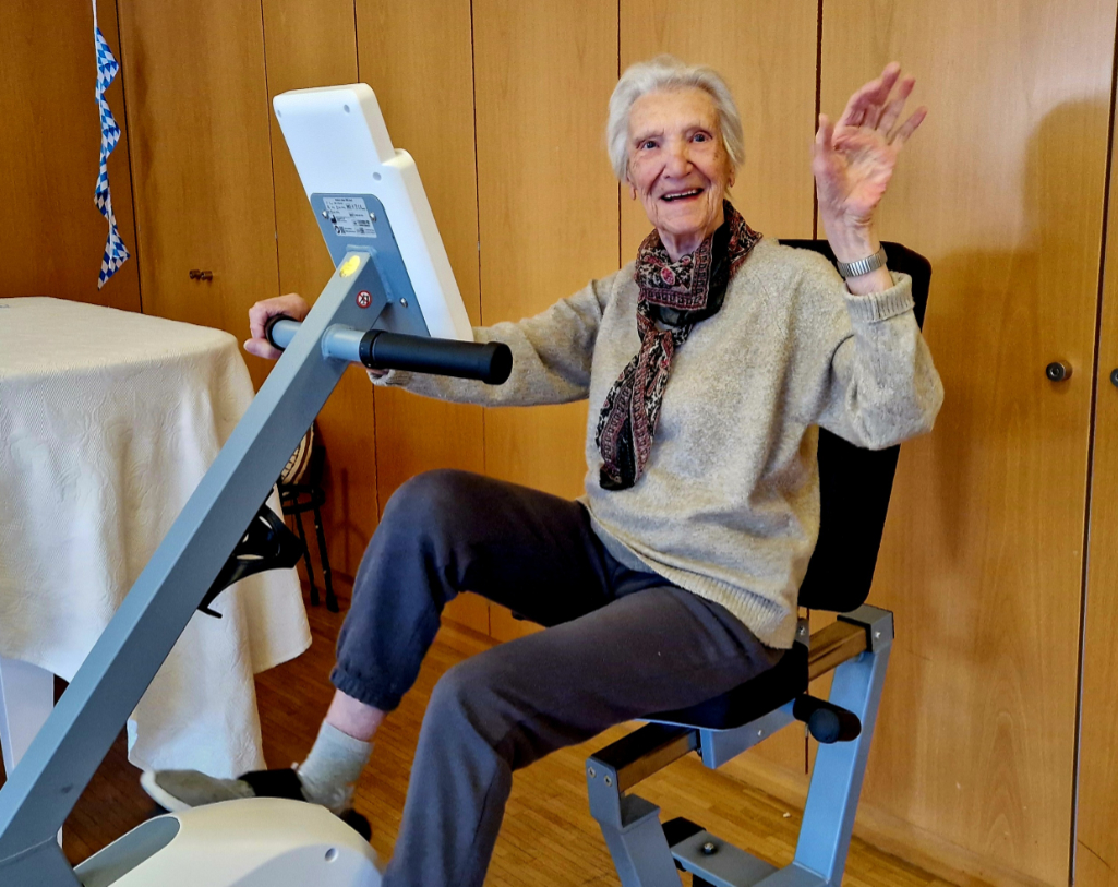 ältere Dame winkt, während sie ein Fitnessgerät benutzt
